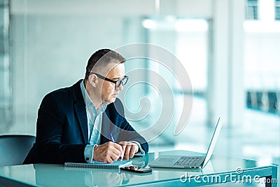Senior financial businessman sitting at his workstation in front of computer and laptop while doing some paperwork. Stock Photo