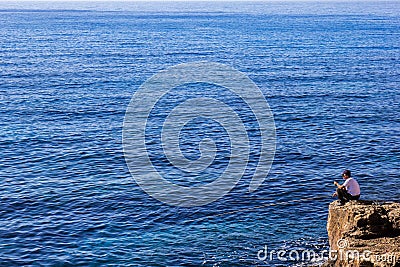 A Senior fisherman on the stone by the ocean Editorial Stock Photo