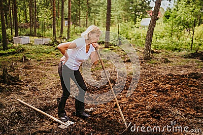 Senior gardener woman falls hurts back pain radiculitis digging at summer farm countryside outdoors using garden tools Stock Photo
