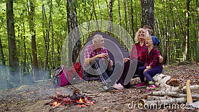 Senior grandmother grandfather granddaughter telling funny stories fairy tales over campfire in wood Stock Photo