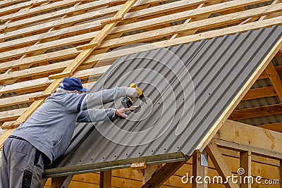 Senior builder man with a screwdriver screwing a roofing sheet to the roof Stock Photo
