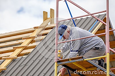 Senior builder man with a screwdriver screwing a roofing sheet to the roof Stock Photo