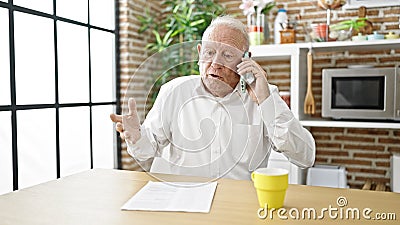 Senior grey-haired man angry arguing on smartphone sitting on table at dinning room Stock Photo