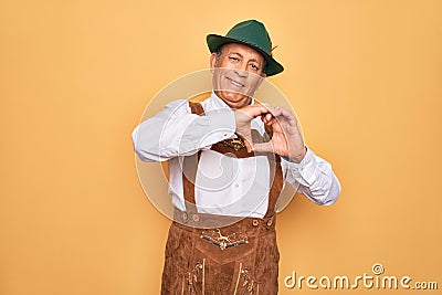 Senior grey-haired man wearing german traditional octoberfest suit over yellow background smiling in love doing heart symbol shape Stock Photo