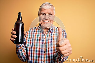 Senior handsome hoary man drinking bottle of beer standing over isolated yellow background happy with big smile doing ok sign, Stock Photo