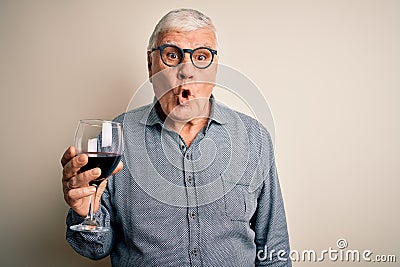 Senior handsome hoary man drinking glass of red wine over isolated white background scared in shock with a surprise face, afraid Stock Photo