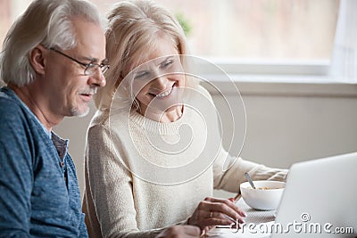 Senior happy couple enjoying using laptop eating breakfast toget Stock Photo