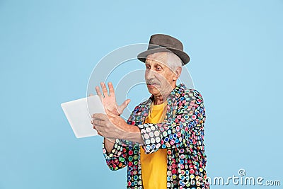 Senior hipster man in stylish hat isolated on blue background. Tech and joyful elderly lifestyle concept Stock Photo