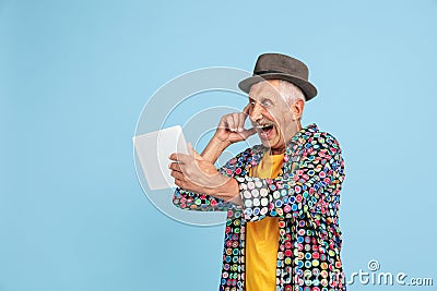 Senior hipster man in stylish hat isolated on blue background. Tech and joyful elderly lifestyle concept Stock Photo