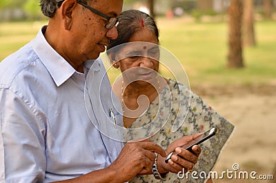 Senior Indian Bengali couple in park looking at their smart phone and smiling in a park in New Delhi, India. Concept love Stock Photo