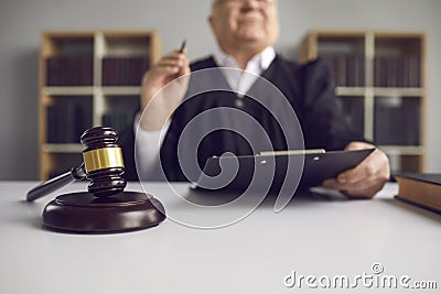 Senior judge with pen and clipboard sit at table shot with focus on mallet Stock Photo