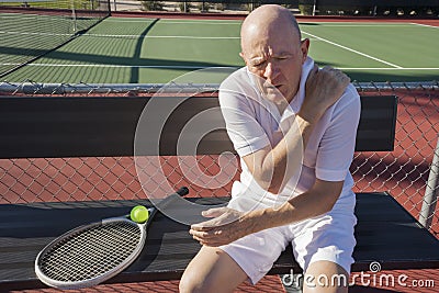 Senior male tennis player with shoulder pain sitting on bench at court Stock Photo