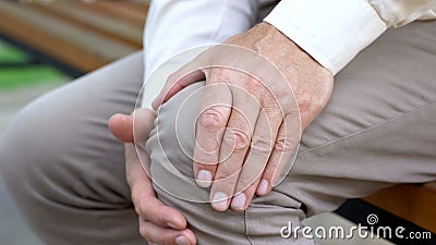Senior male touching knee, sitting on bench, pain in joints, problems with knees Stock Photo