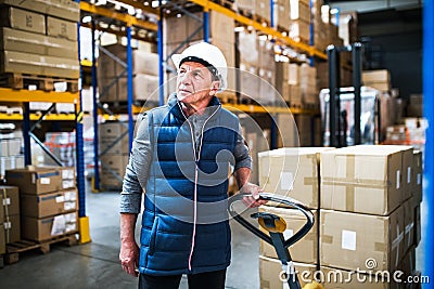 Senior male warehouse worker pulling a pallet truck. Stock Photo