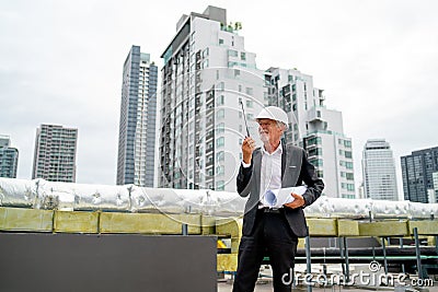 Senior man as professional engineer or technician use walkie talkie and stand near line of air vents on rooftop of construction Stock Photo