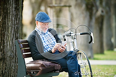 Senior man with bicycle in town, holding smart phone, texting Stock Photo