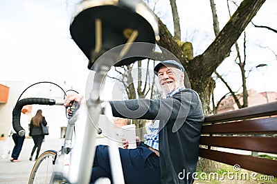 Senior man with bicycle in town, sitting on bench, drinking coff Stock Photo