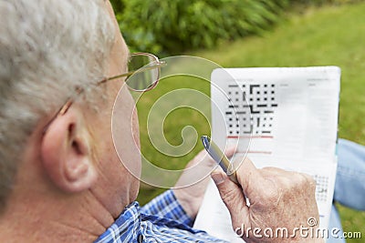 Senior Man Doing Crossword Puzzle In Garden Stock Photo