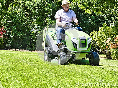 Senior man driving a tractor lawn mower in garden with flowers Stock Photo