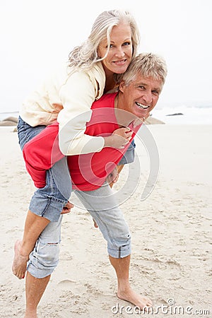 Senior Man Giving Woman Piggyback On Winter Beach Stock Photo