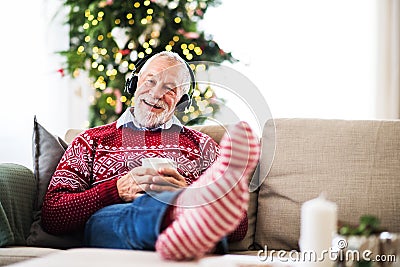 A senior man with headphones listening to music at home at Christmas time. Stock Photo