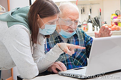 Senior man is helped by his caregiver to using laptop at home during Coronavirus Pandemia Stock Photo