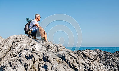 Senior man hiking looking at sea landscape sitting on rocks Stock Photo