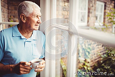 Senior man holding cup and looking out of the window Stock Photo