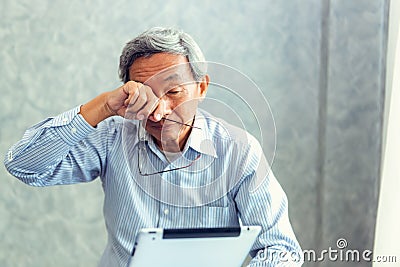 Senior man is holding eyeglasses and rubbing his tired eyes whi Stock Photo