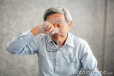 Senior man is holding eyeglasses and rubbing his tired eyes whi Stock Photo