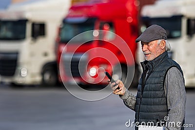 Senior man logistician with phone standing in front of trucks Stock Photo