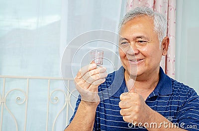 senior man looking at medicine in his hand and showing with thumb up to the side with happy face smiling at home or hospital Stock Photo