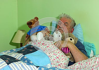 Senior man asleep in bed with soft cuddly toys. Stock Photo