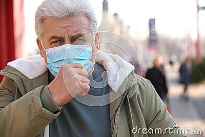 Senior man with medical mask coughing on street. Virus protection Stock Photo