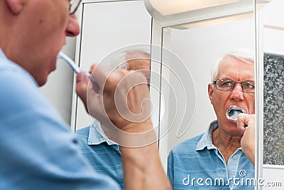 Senior man in mirror brushing his teeth Stock Photo