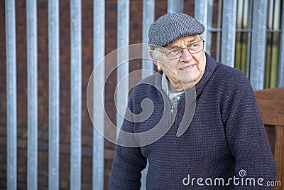 Senior man resting on a wooden bench infront of metal fence Stock Photo