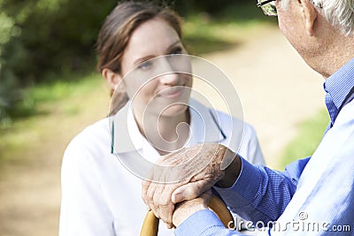 Senior Man's Hands Resting On Walking Stick With Care Worker In Stock Photo