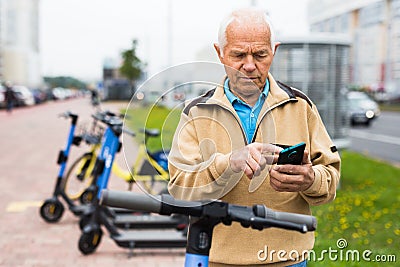 Senior man with smartphone activating electric scooter Stock Photo