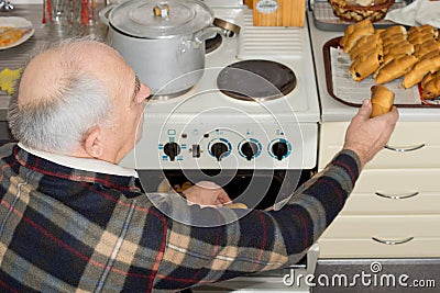 Senior man taking a bread roll out of the oven Stock Photo