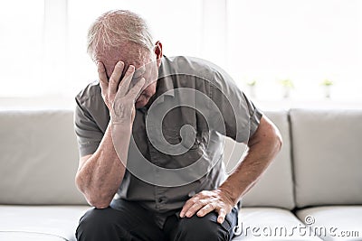 Senior man thinking and sitting on sofa at home like sad Stock Photo