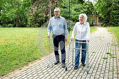 Senior man using a walking cane accompanied by a senior lady strolling with folding walker Stock Photo