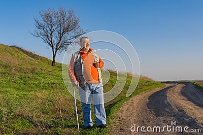 Senior man with walking stick standing on an earth road Stock Photo