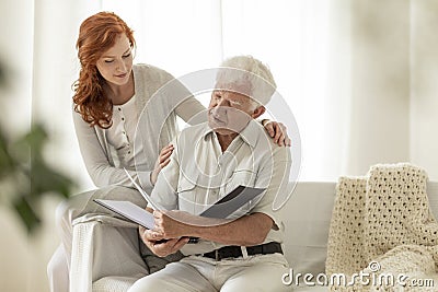 Senior man watching photo album during visit of granddaughter at Stock Photo