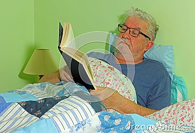 Senior man reading in bed. Stock Photo