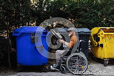 Senior man in wheelchair throwing paper waste, cardboard into recycling container in front his apartment. Elderly man Stock Photo