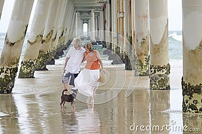 Senior man and woman enjoying a romantic relaxing holiday at beach with pet dog Stock Photo