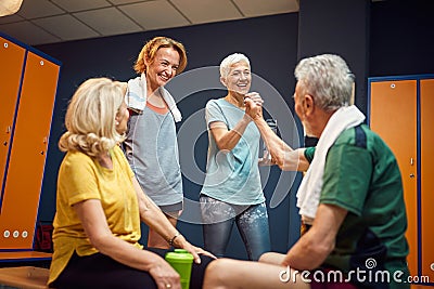 Senior man and woman high fiving in gym locker room, feeling energized for workout, mature woman and young woman cheering for them Stock Photo