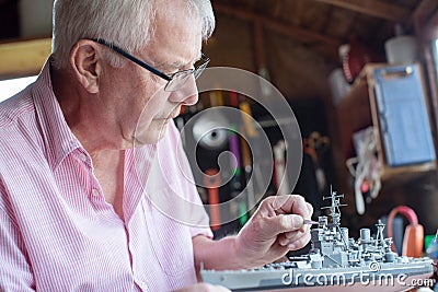 Senior Man Working On Model Ship In Shed At Home Stock Photo
