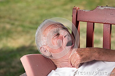 Senior man yawning in garden on bench Stock Photo