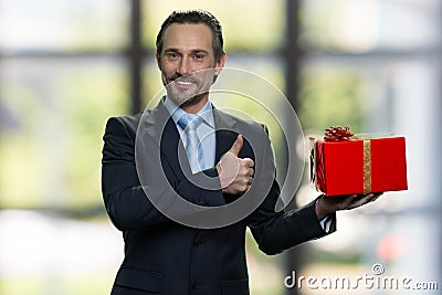 Senior manager with red gift box and showing thumb up. Stock Photo